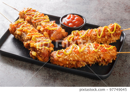 Korean corn dogs or Korean hot dogs are popular local street food, typically made of sausages or mozzarella cheese on sticks deep-fried closeup on the plate. Horizontal 97749045