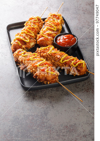 Korean corndogs Korean street food it consists of mozzarella cheese and hotdog skewered then battered and fried to golden brown perfection closeup on the plate. Vertical 97749047