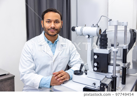 Male doctor working on optometric equipment at clinic 97749454