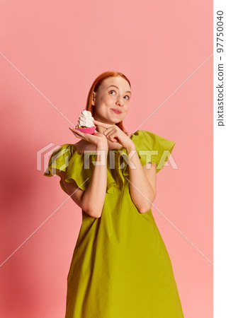 Portrait of young beautiful girl in cute dress posing with cupcake over pink background. Cute, dreamy look Portrait of young beautiful girl in cute dress posing with cupcake over pink background. Cute, dreamy look 97750040