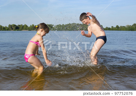 Children splash water on the banks of the river, in the beach season. Summer holidays with children Children splash water on the banks of the river, in the beach season. Summer holidays with children 97752076