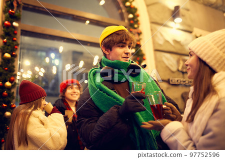Emotional young people, friends meeting, smiling, drinking hot drinks at evening city street at winter time. Emotions, love, friendships, ad, sales concept Emotional young people, friends meeting, smiling, drinking hot drinks at evening city street at winter time. Emotions, love, friendships, ad, sales concept 97752596