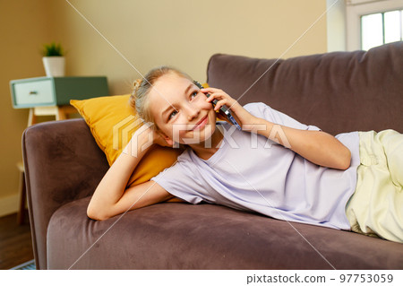 cute little girl useing smartphone and lying down on sofa in viving room at her home 97753059