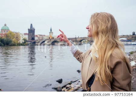 woman with an appetite eats a traditional The Charles Bridge feed the swans with trdlo or trdelnik in Prague sity in Chezh 97753164