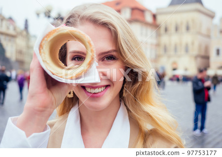 woman with an appetite eats a traditional Czech sweet Trdelnik in Prague street 97753177