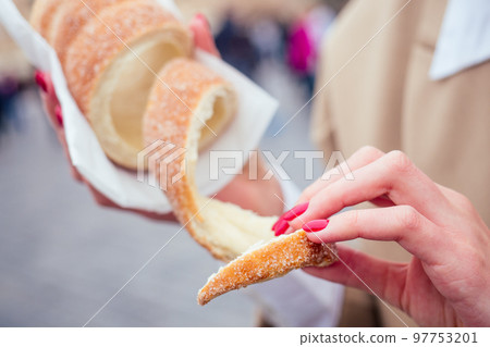woman with an appetite eats a traditional Czech sweet Trdelnik in Prague street 97753201