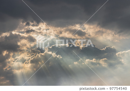 The sun's rays passing through the clouds and shining form an interesting light pattern against the sky. 97754540
