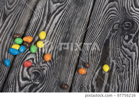 Chocolate candy in multi-colored glaze. Scattered on black pine boards. Chocolate candy in multi-colored glaze. Scattered on black pine boards. 97756216