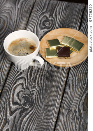 A cup of black coffee in a white cup. Chocolate in foil. On pine boards. 97756230