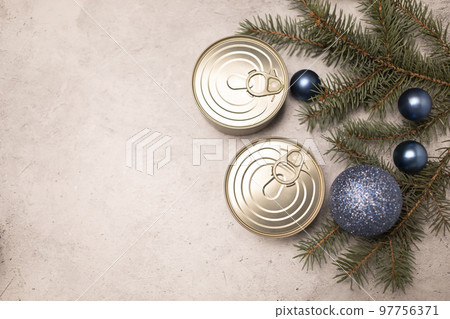 Christmas canned products, preservation, packed fish, meat or vegetables in can on concrete gray background with Christmas tree and toy balls. Space for text. New year food concept. Horizontal 97756371