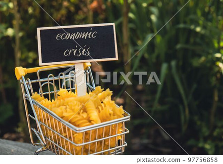 ECONOMIC CRISIS text on Blackboard label Shopping trolley cart Filled With Pasta on agriculture background. Food and groceries shopping price increase, Rising food cost food crisis inflation 97756858