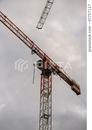 Silhouettes of construction cranes and unfinished residential building against the sunrise above the city. Housing construction, apartment block Construction of new residential high-rise buildings 97757117