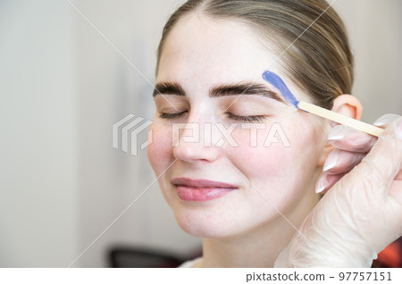 Eyebrow correction. The master applies wax with a wooden spatula. Eyebrow correction. The master applies wax with a wooden spatula. 97757151