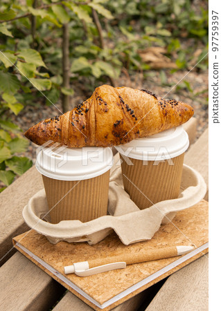 Fresh baked chocolate croissant on Two paper cups with lid for tea to go. Empty paper notebook. Freelancer's place of work. Study and work online. Remote business education. Making plans for next week Fresh baked chocolate croissant on Two paper cups with lid for tea to go. Empty paper notebook. Freelancer's place of work. Study and work online. Remote business education. Making plans for next week 97759397