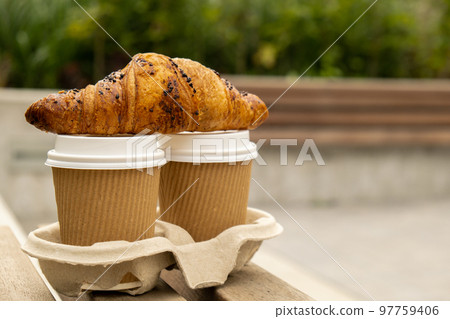 Fresh baked chocolate croissant on Two paper cups with lid for tea to go. Breakfast Coffee take away on the table. Take-out coffees with brown paper cup holder. Brown safety cardboard collars Fresh baked chocolate croissant on Two paper cups with lid for tea to go. Breakfast Coffee take away on the table. Take-out coffees with brown paper cup holder. Brown safety cardboard collars 97759406