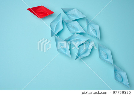 Group of blue paper boats heading in one direction and one red one heading in the opposite direction. The concept of individuality, uniqueness and talent of the employee. 97759550