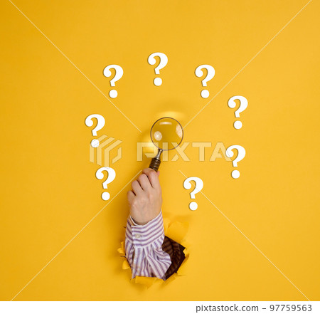 Female hand holds a magnifying glass on a yellow background, part of the body sticks out of a torn hole in a paper background. Business concept, finding information, answering questions 97759563