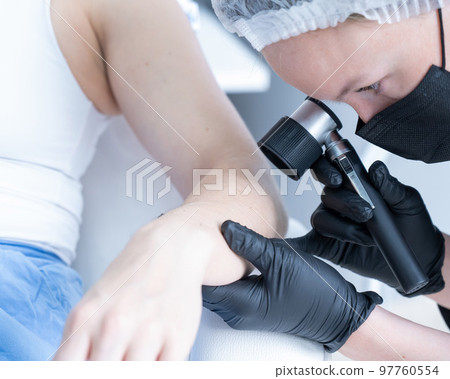 A dermatologist examines a patient's mole through a dermatoscope. A dermatologist examines a patient's mole through a dermatoscope. 97760554