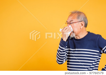 Pensioner unwell. Asian older man cold having flu and sneezing from sickness virus problem use tissue paper, Portrait senior old man blowing nose with tissue studio shot isolated on yellow background Pensioner unwell. Asian older man cold having flu and sneezing from sickness virus problem use tissue paper, Portrait senior old man blowing nose with tissue studio shot isolated on yellow background 97760579