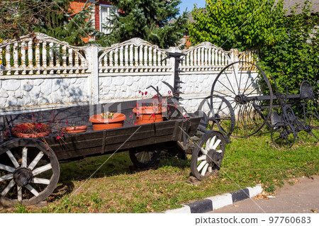 Old peasant exhibits in landscape design. An old wooden cart and forged tools for agriculture Old peasant exhibits in landscape design. An old wooden cart and forged tools for agriculture 97760683