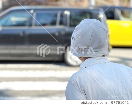 An elderly woman standing in front of a pedestrian crossing and a car going back and forth 97761041