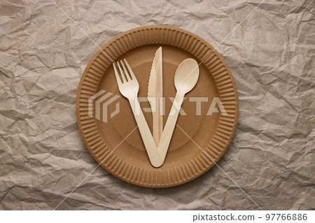 Wooden fork, spoon and knife on cardboard plate on crumpled paper Wooden fork, spoon and knife on cardboard plate on crumpled paper 97766886