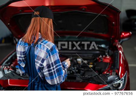 Caucasian female auto mechanic uses a special computer to diagnose faults.  97767656