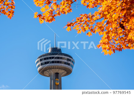 Niagara Falls, Ontario, Canada - October 27 2022 : Skylon Tower, autumn maple leaves over blue sky. Fall foliage in Niagara Falls City. 97769545