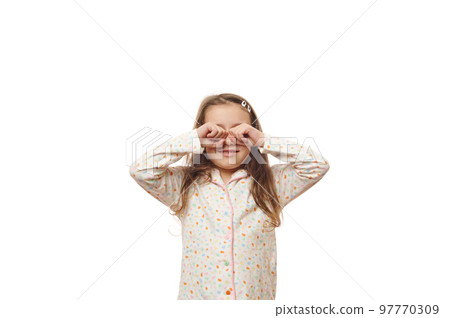 Adorable Caucasian little child, happy baby girl with long hair, wearing comfortable cotton pajamas, rubbing eyes when waking up, isolated over white background. Copy advertising space Adorable Caucasian little child, happy baby girl with long hair, wearing comfortable cotton pajamas, rubbing eyes when waking up, isolated over white background. Copy advertising space 97770309