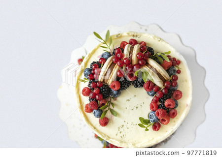 Top view of light coloured birthday cake decorated with fresh berries and macaroons cake. Beautiful dessert on white background Top view of light coloured birthday cake decorated with fresh berries and macaroons cake. Beautiful dessert on white background 97771819