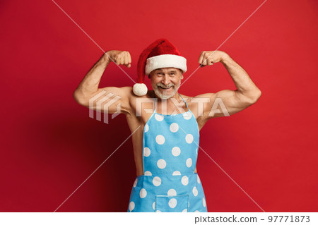 Senior Man Showing Biceps. Strong Bearded Man In Santa Hat And Apron Senior Man Showing Biceps. Strong Bearded Man In Santa Hat And Apron 97771873