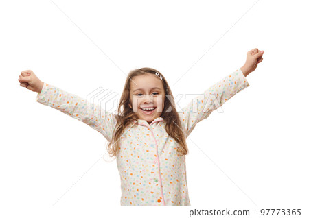 Cheerful baby girl in white pyjama with colorful dots, raising arms up, rejoicing, expressing amazement and happiness, smiling looking at camera, on white background. Space for your advertising text Cheerful baby girl in white pyjama with colorful dots, raising arms up, rejoicing, expressing amazement and happiness, smiling looking at camera, on white background. Space for your advertising text 97773365