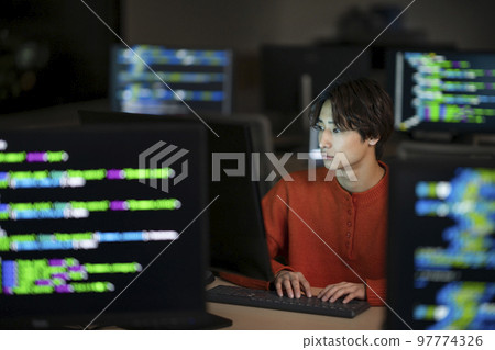 一名被 PC 顯示器包圍的年輕人 一名工程師晚上在辦公室工作的圖片 97774326