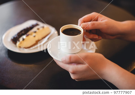 close up mug of coffee in the hands and a sweet dessert on a plate close up mug of coffee in the hands and a sweet dessert on a plate 97777907