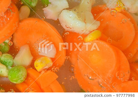 Close-up fresh soup vegetables with carrots, peas, cauliflower and corn on white background. Soup vegetables with carrots, peas, cauliflower and corn in boiling water on white background, close-up 97777998