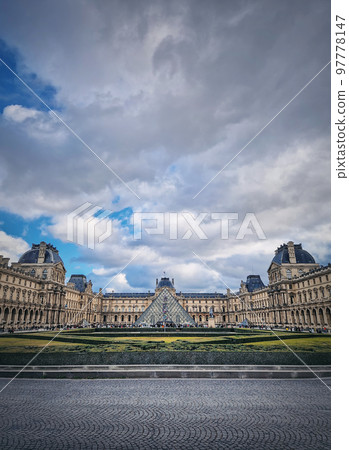 Outdoors view to the Louvre Museum in Paris, France. The historical palace building with the modern glass pyramid in center, vertical background 97778147