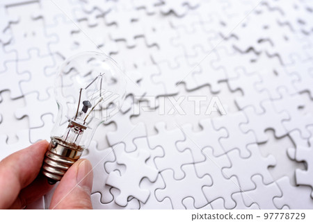 A hand holding a light bulb that sparks an idea Background texture of a disjointed jigsaw puzzle Strategy Standard color 97778729