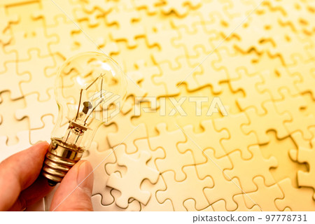 A hand holding a light bulb that sparks an idea Background texture of a disjointed jigsaw puzzle Strategy Gold 97778731