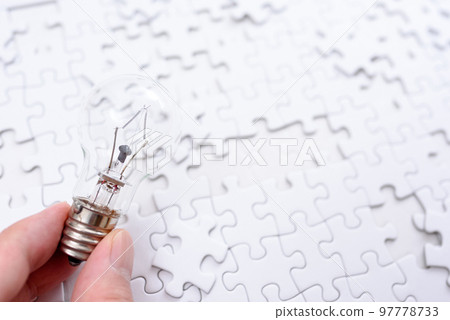 A hand holding a light bulb that sparks an idea Background texture of a disjointed jigsaw puzzle Strategy bright 97778733