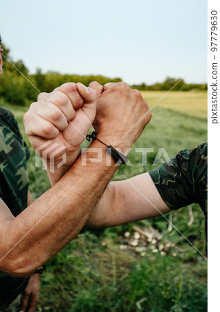 The hand of a civilian man and the hand of a Ukrainian military man on the background of a field. The hand of a civilian man and the hand of a Ukrainian military man on the background of a field. 97779630