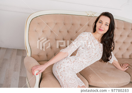 fashion portrait of a young beautiful woman in a lace elegant white dress posing in a studio, positive and happy 97780283