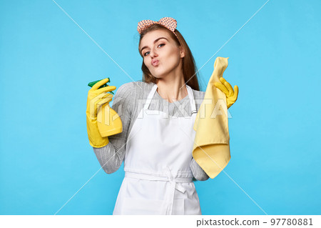 caucasian woman in yellow rubber gloves and cleaner apron with sponge and detergent sprayer caucasian woman in yellow rubber gloves and cleaner apron with sponge and detergent sprayer 97780881