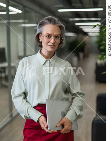 Mature caucasian woman stands with a laptop among the office. Mature caucasian woman stands with a laptop among the office. 97780900