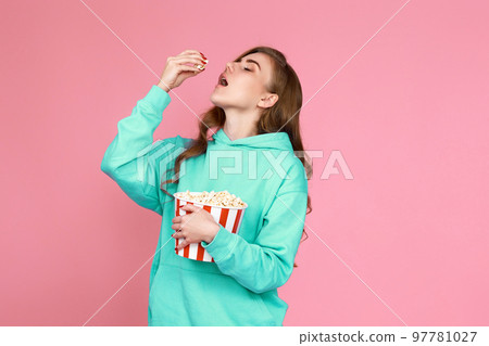 woman in sweatshirt watching movie film, eating popcorn 97781027