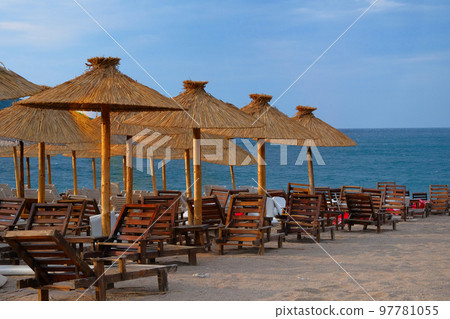 Beach chairs and straw umbrellas on tropical resort. Line of lounge chairs. Blue sea and sky on background. Summer vacations concept. 97781055
