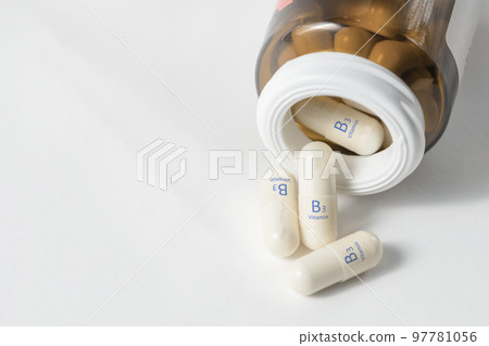 Vitamin B3. Vitamins in capsules. White capsules with vitamin B3, niacinamide or nicotinic acid are scattered on the table from a bottle on a white background. Dietary supplements in tablets. 97781056