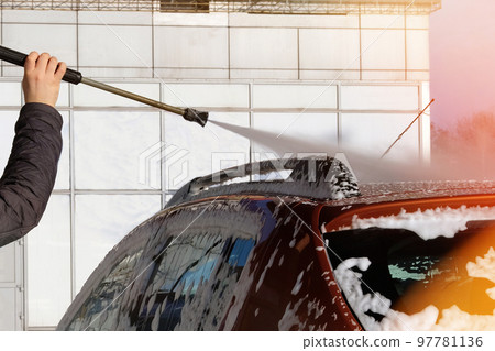 Car is cleaning with soap suds at self-service car wash. White soap suds on auto. Sunlight. 97781136