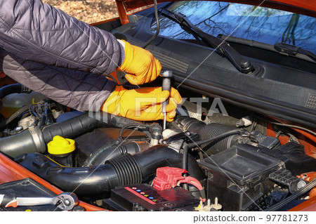 Car maintenance and repair concept. Hands of driver in orange rubber gloves checks car using tools, open hood. Automobile and transportation, close up. 97781273