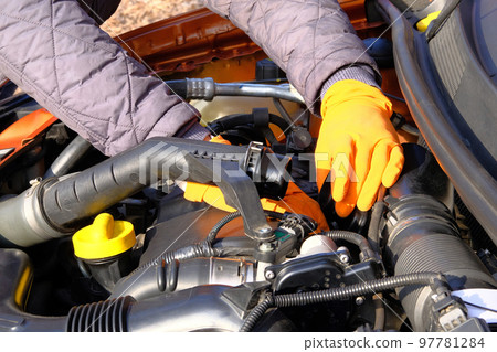 Automobile maintenance concept. Hands of driver in orange rubber gloves checks car, open hood. Cars and transportation, close up. 97781284