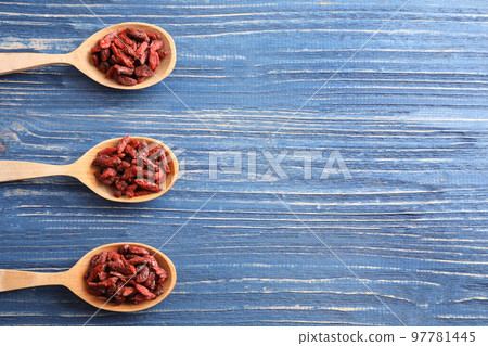 Dried goji berries in spoons on blue wooden table, flat lay. Space for text 97781445
